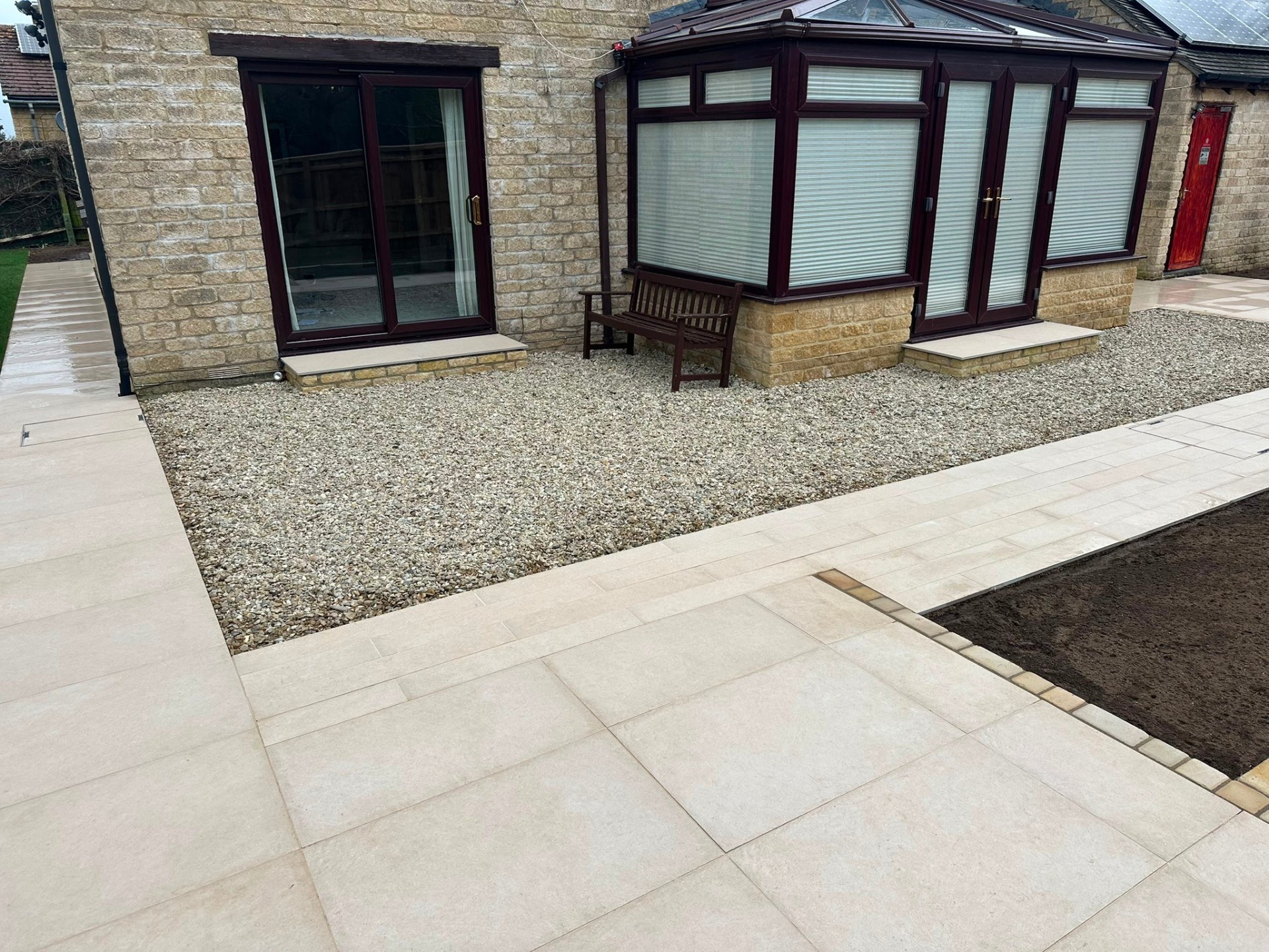 Contemporary cream porcelain patio and garden path with decorative gravel and stone walling.