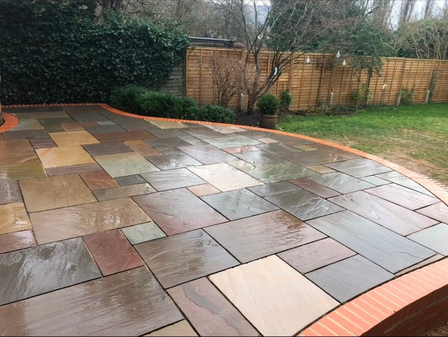 Riven natural stone patio with multi-colour sandstone flags and red brick edging