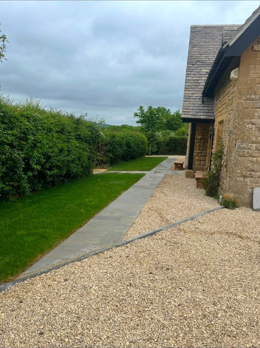 Natural stone garden path alongside a Cotswold stone building with lawn and gravel borders.