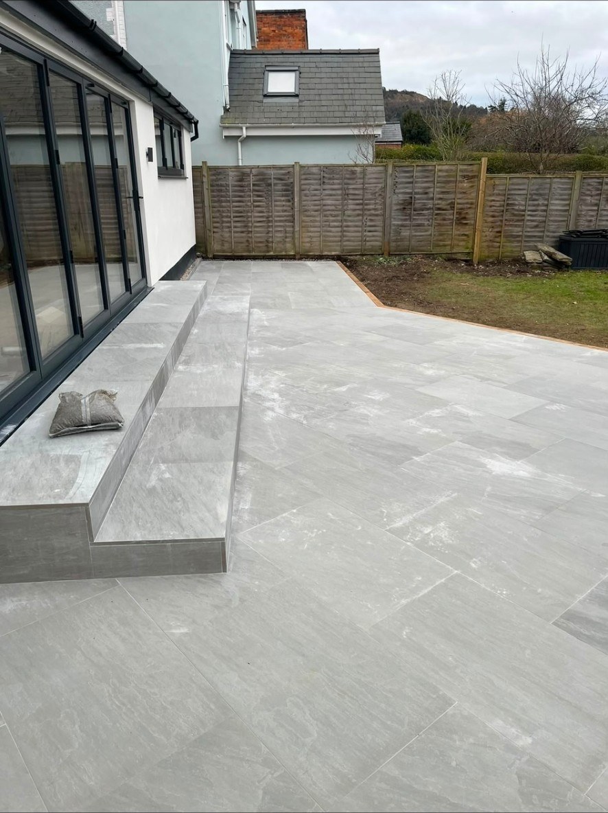 Contemporary light grey porcelain paving patio with integrated steps outside bifold doors.