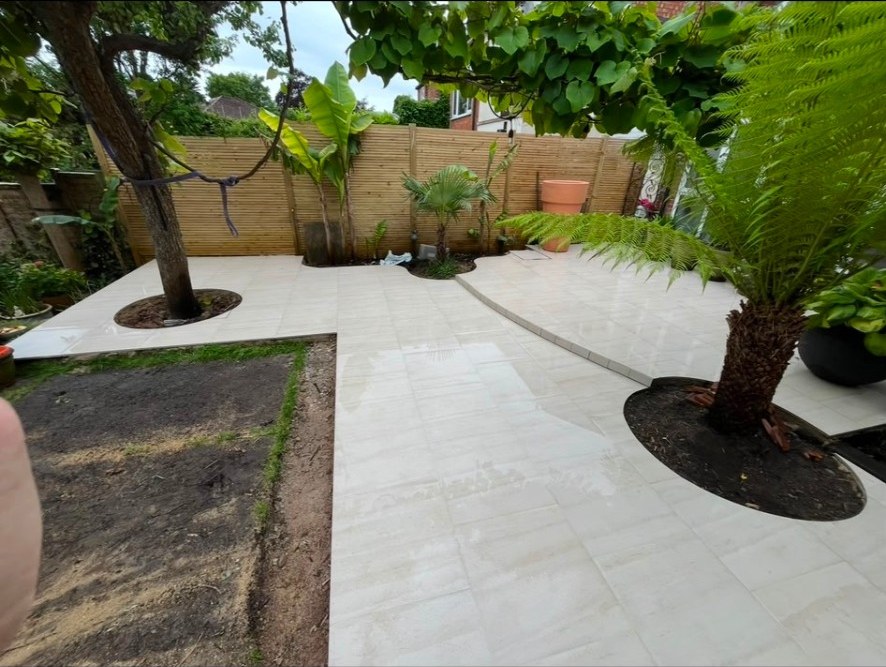 Contemporary light cream porcelain patio with circular tree cutouts and slatted timber fencing.