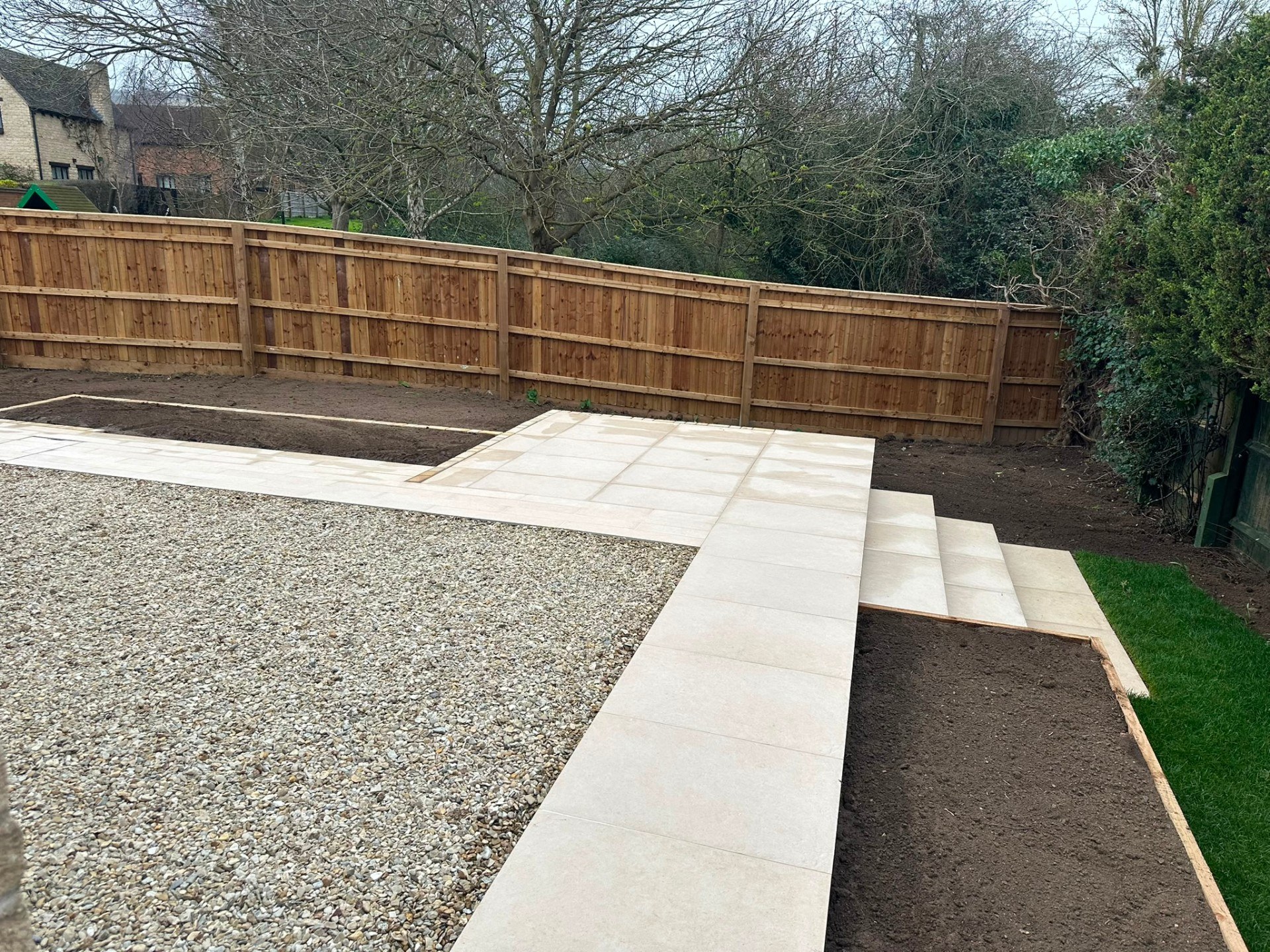 Contemporary porcelain tile path and patio steps bordering a garden gravel area and timber fence.