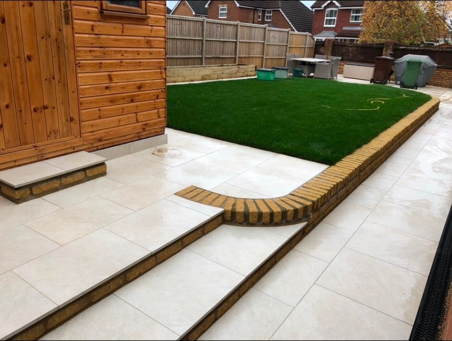 Contemporary garden with light porcelain patio, raised brick borders, timber shed and new lawn.