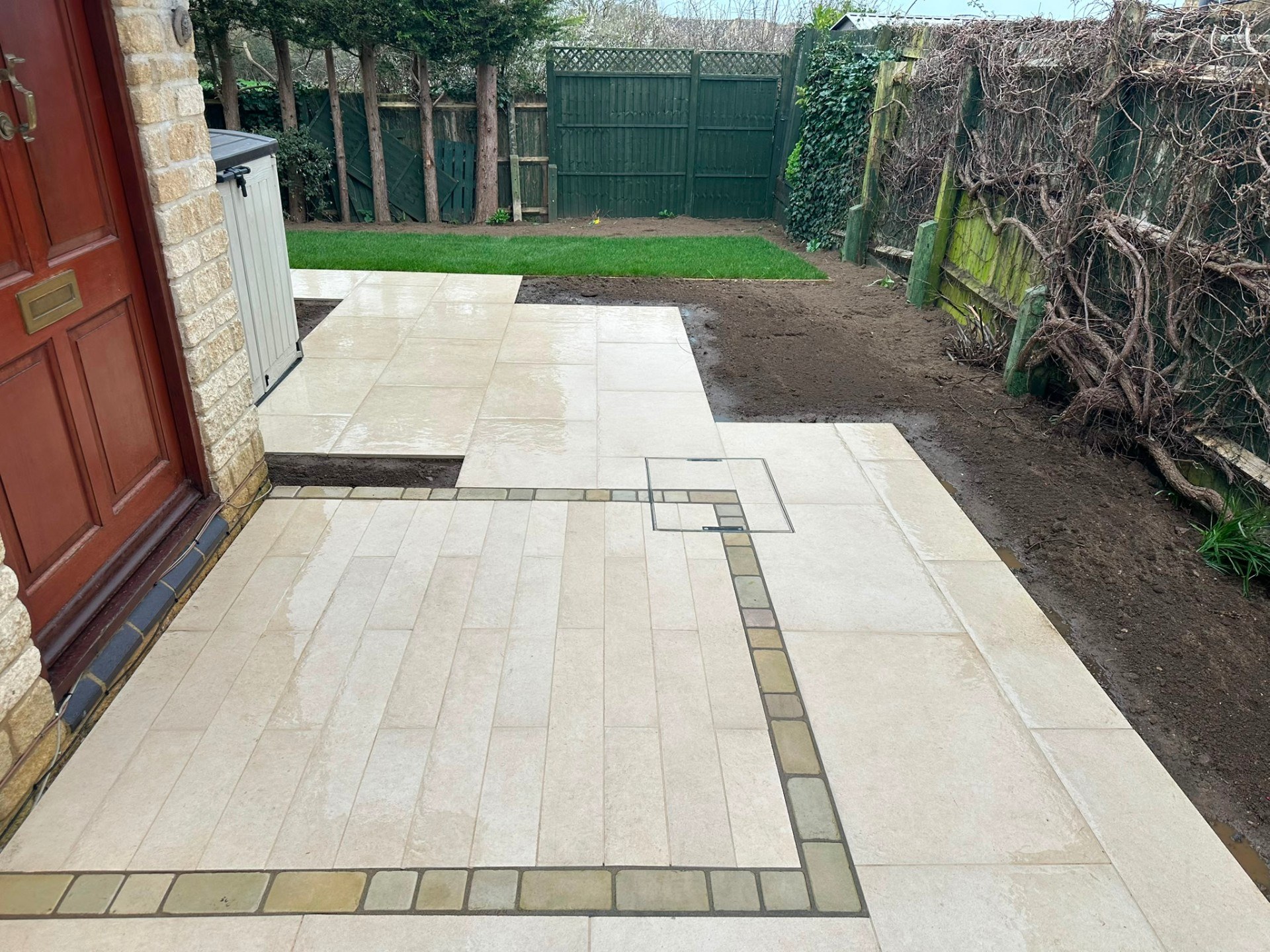 Contemporary light porcelain patio with setts border and recessed manhole cover tiling.