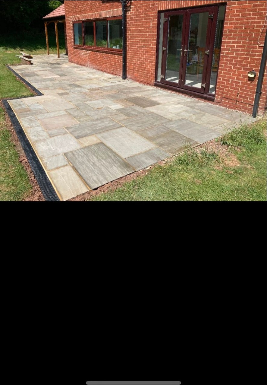 Natural sandstone flags laid as a garden patio next to a red brick house.