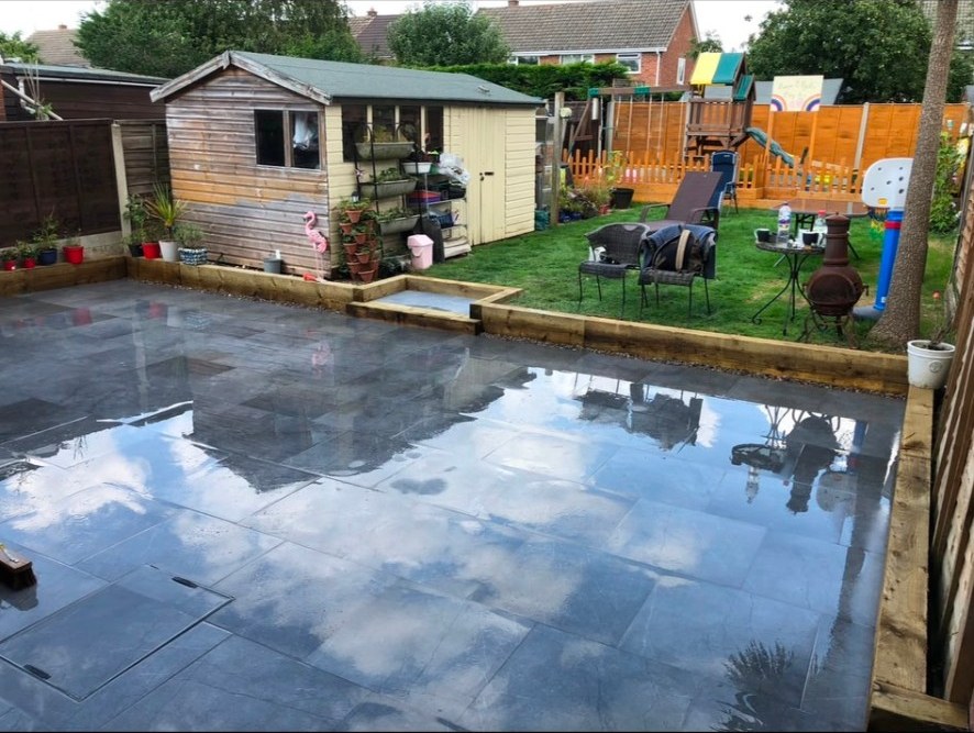 Wet limestone flagstone patio with timber sleeper retaining wall in a suburban back garden.