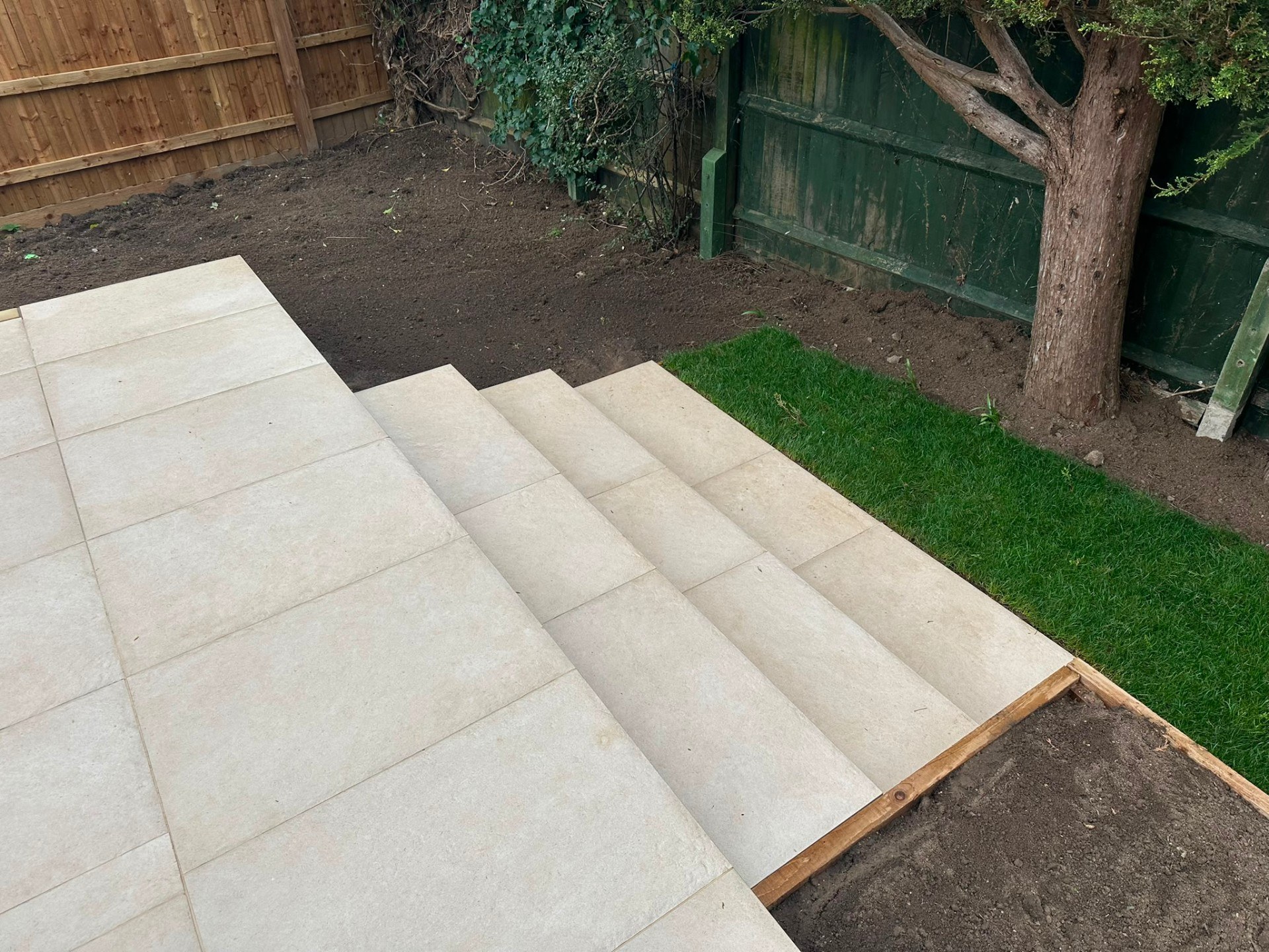 Modern beige porcelain paving patio and tiered steps in a back garden.