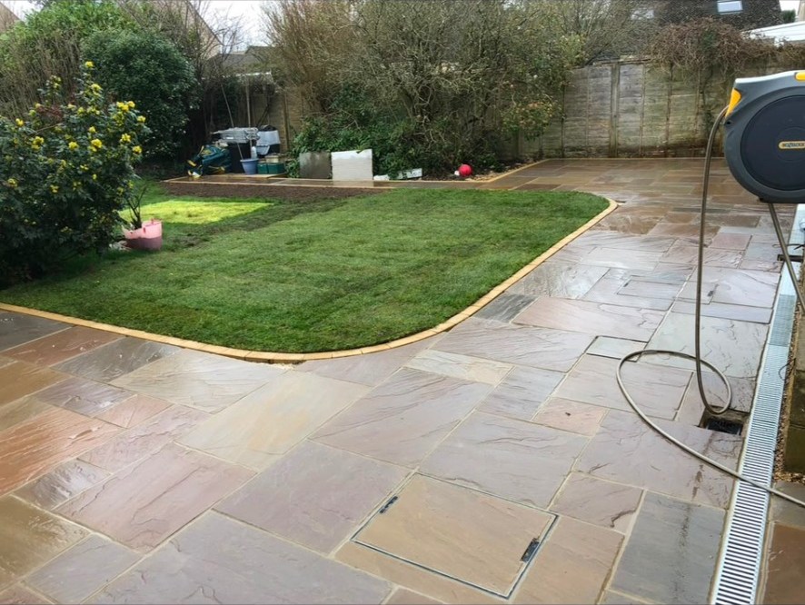 Riven natural stone patio wrapping around a fresh turf lawn with block edging.