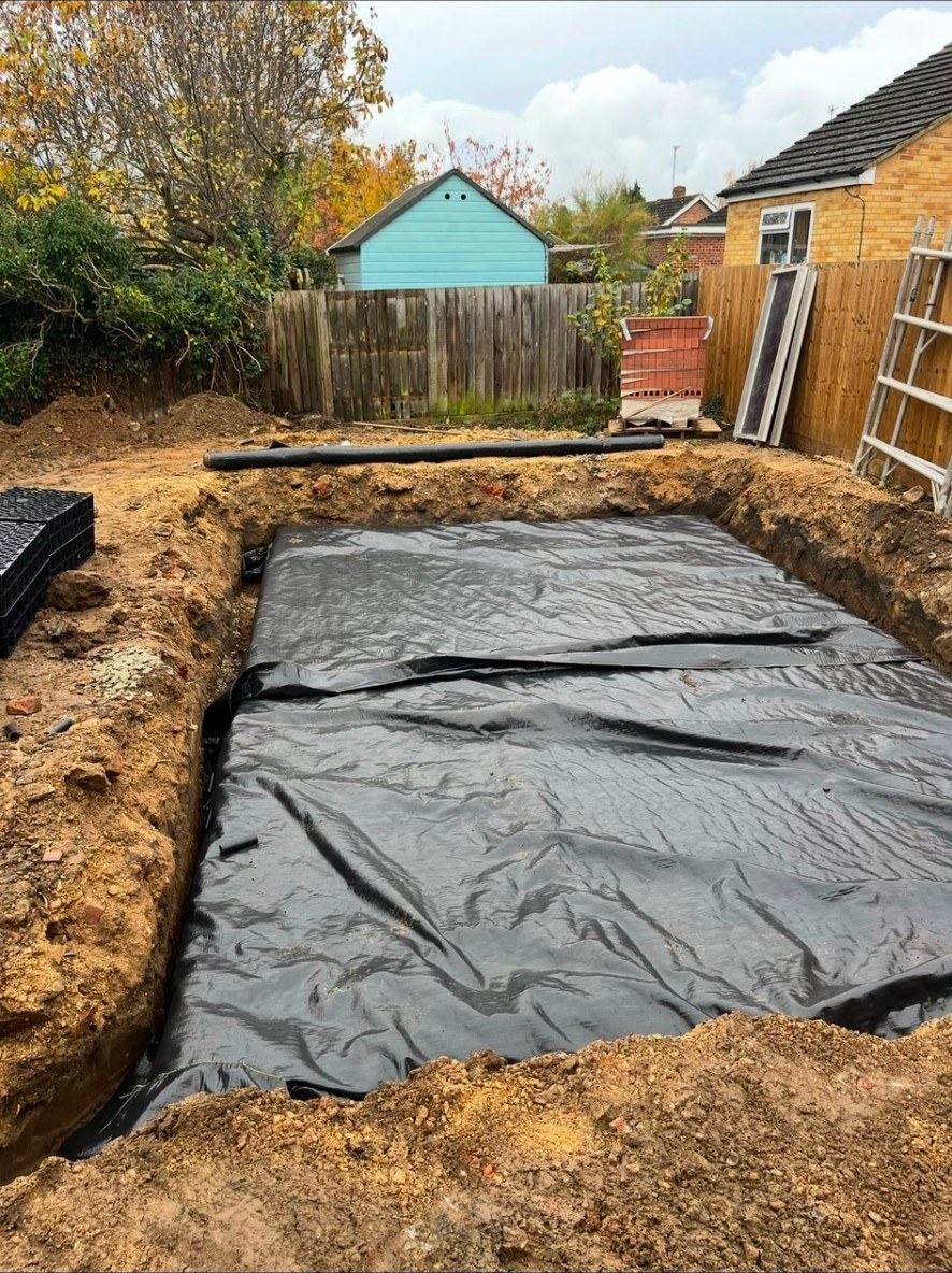 Groundworks showing a deep excavation with a geotextile membrane and drainage crates in a garden.