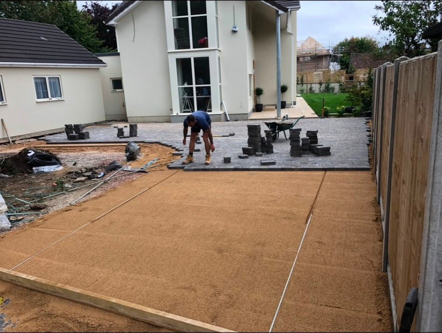 Work in progress of grey block paving being laid on a prepared sand sub-base for a patio.