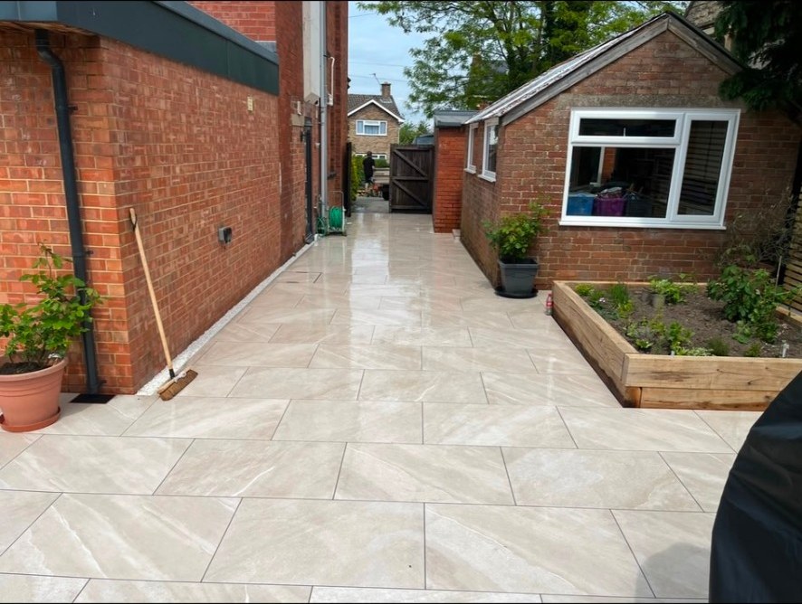 Contemporary beige porcelain patio and side path alongside a brick house and raised sleeper bed.