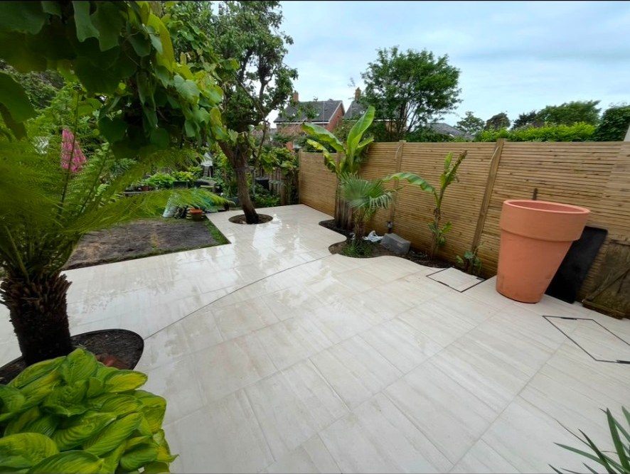Contemporary garden with wet porcelain patio, slatted timber fencing, and tropical planting.