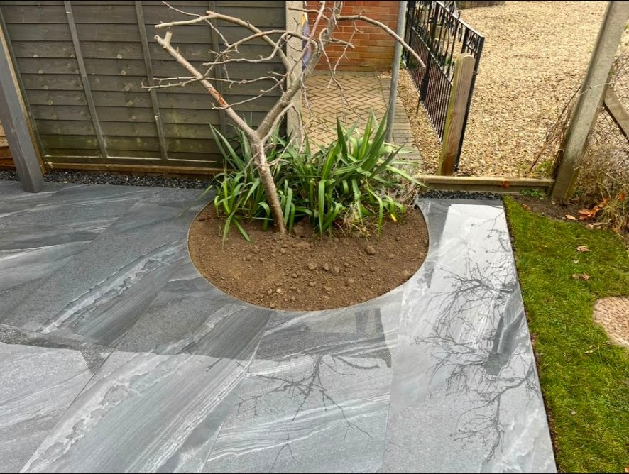 Contemporary grey porcelain patio with a precision-cut circular plant bed feature.