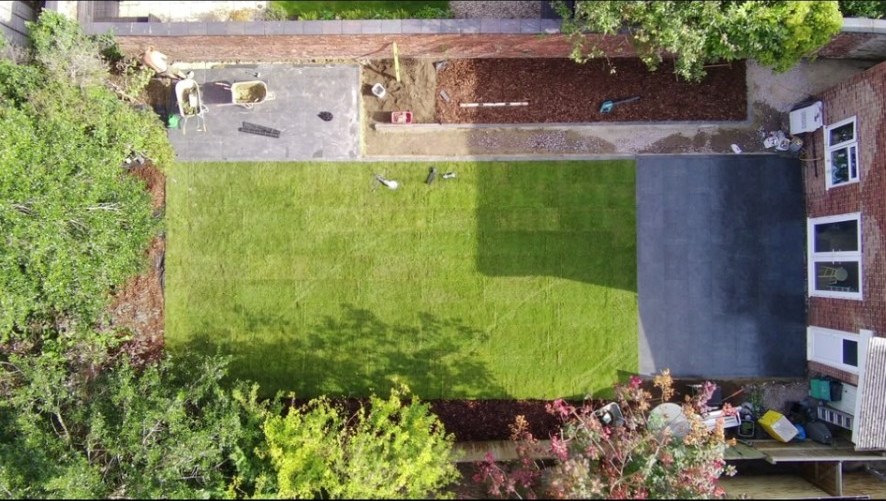 Aerial view of garden renovation with dark porcelain patio, new turf lawn and flower beds.