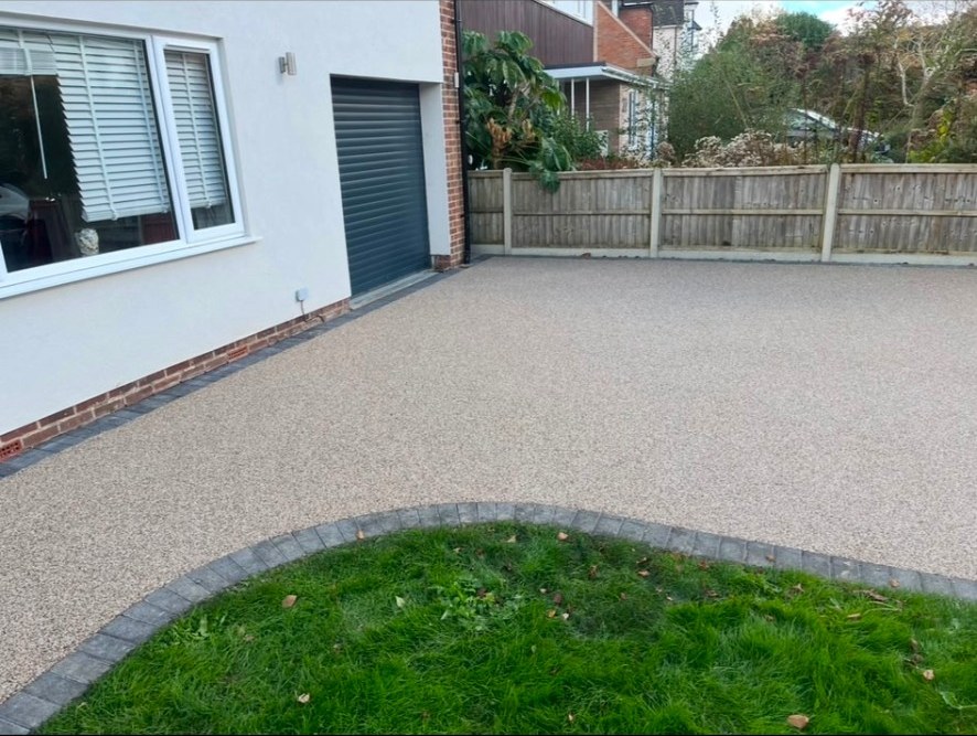 Seamless resin bound driveway with dark grey block paving border by a white house and garage.