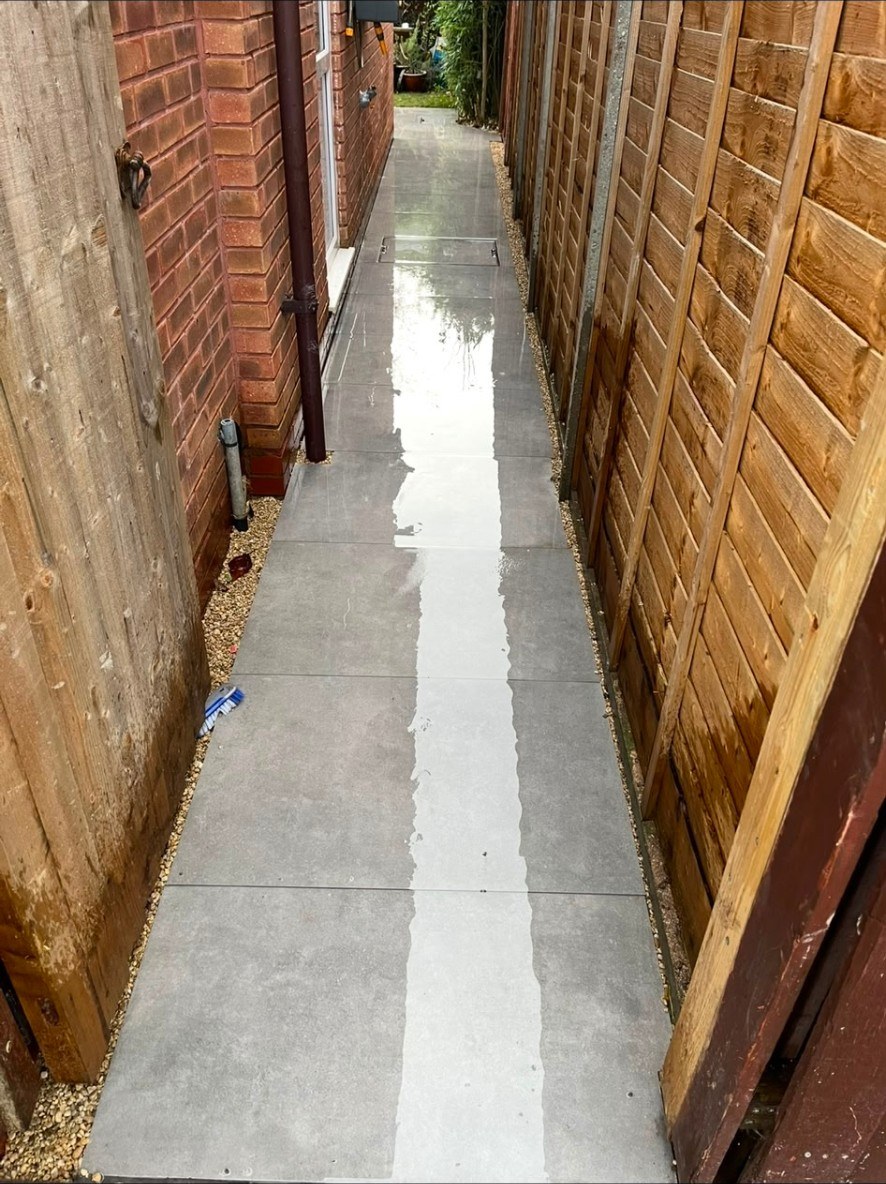 Modern grey porcelain paving path in a narrow side garden alley with timber fencing.