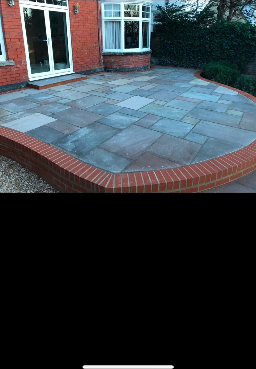 Natural stone paving patio with a curved red brick retaining wall border.